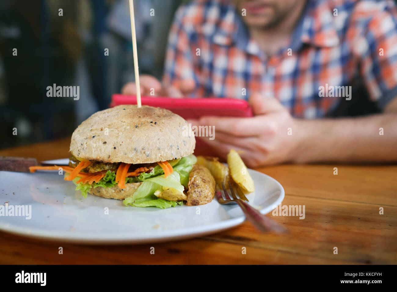 Veggie patata dolce burger con verdure fresche servita su piastra bianca. sfocato uomo caucasico seduta sullo sfondo Foto Stock