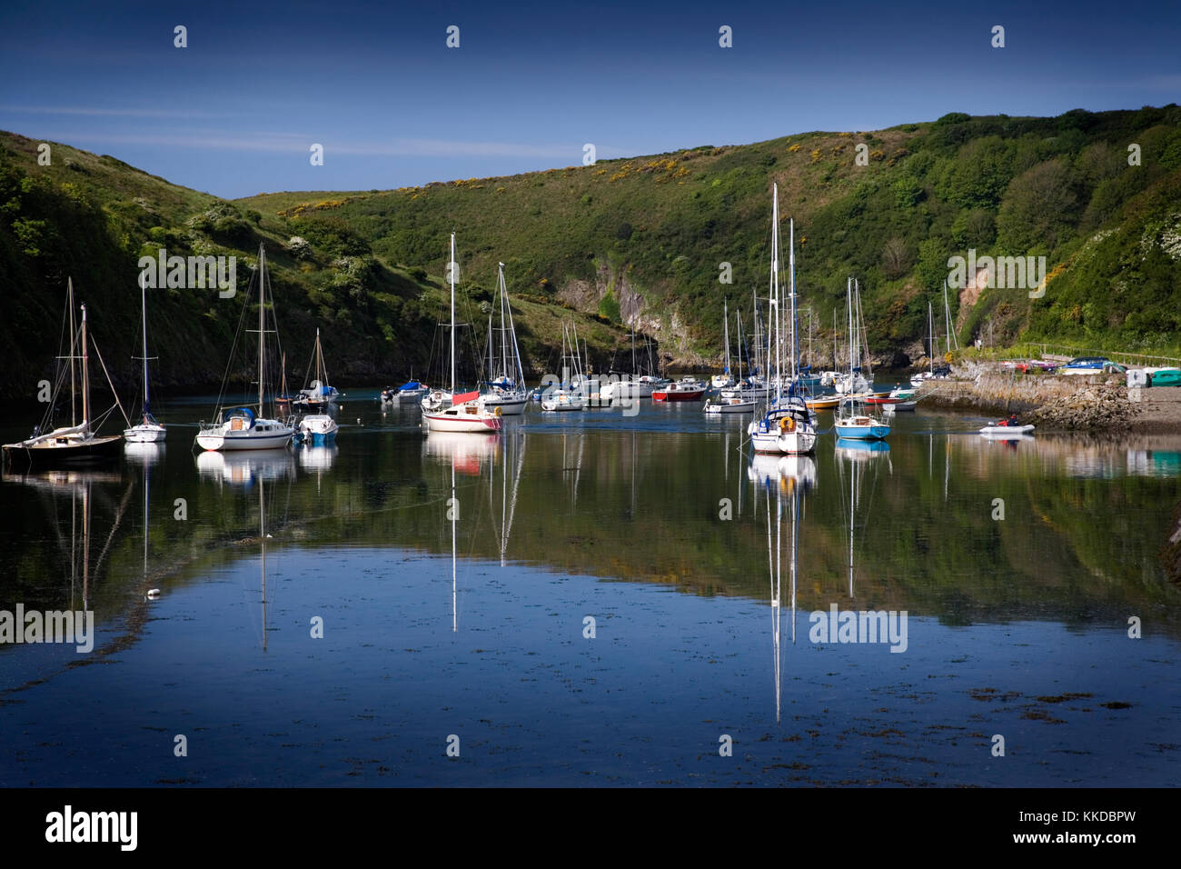 Solva Harbour, Pembrokeshire, Wales, Regno Unito con piccole imbarcazioni al dispositivo di ancoraggio e di riflessioni nel perfettamente ancora acqua su una bella mattina d'estate Foto Stock