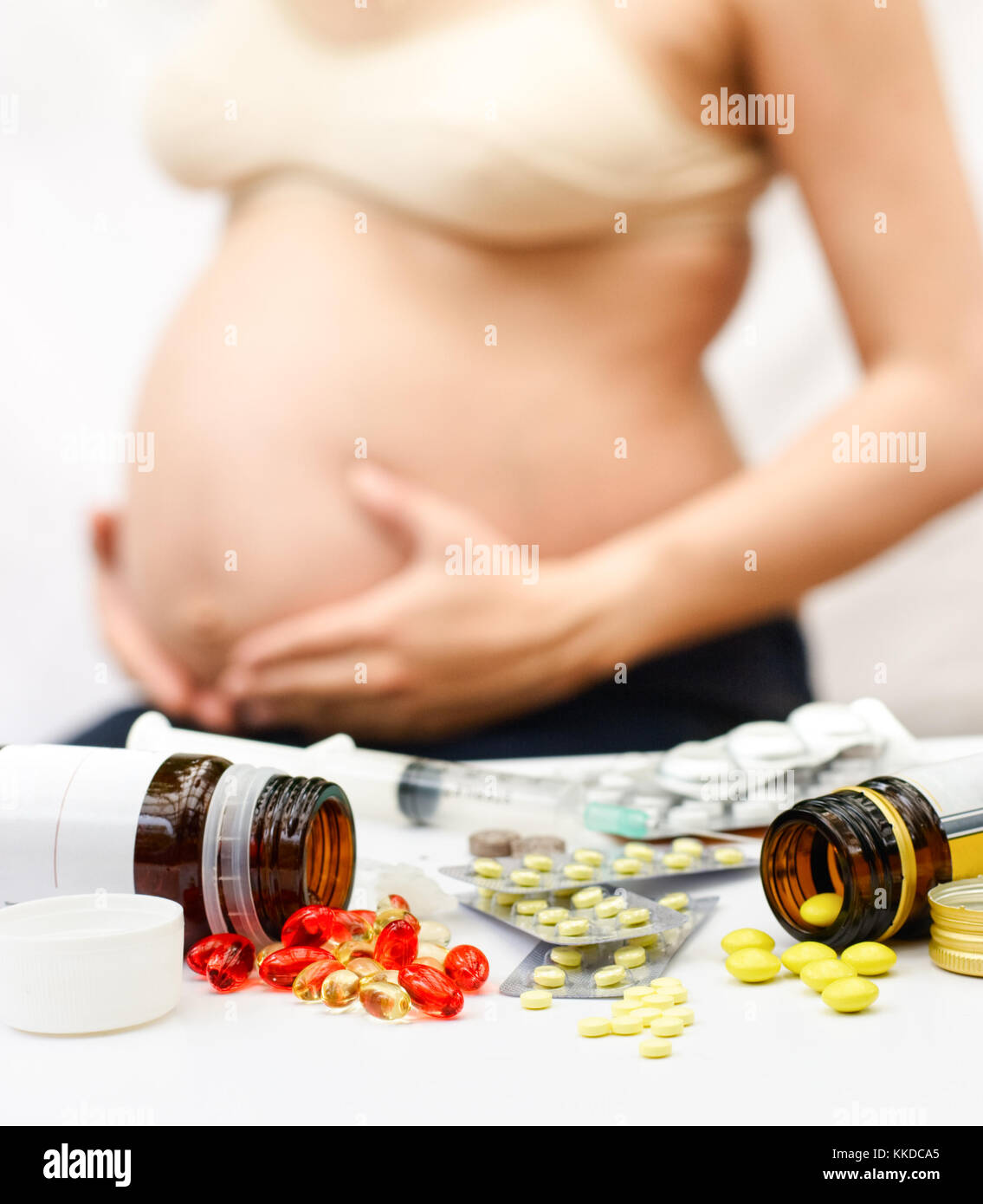 Giallo e rosso pillole fuoriuscita dalle bottiglie e blister nella parte anteriore della donna incinta, shallow dof Foto Stock