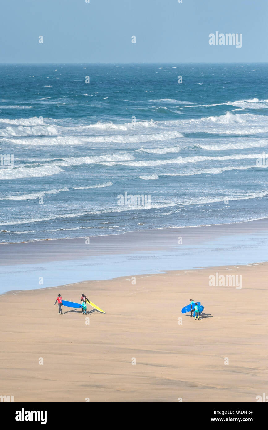 Surf - istruttori di una scuola di surf scuola di surf e giovani studenti a piedi al mare e trasportare le loro tavole da surf a Fistral Beach Newquay. Foto Stock