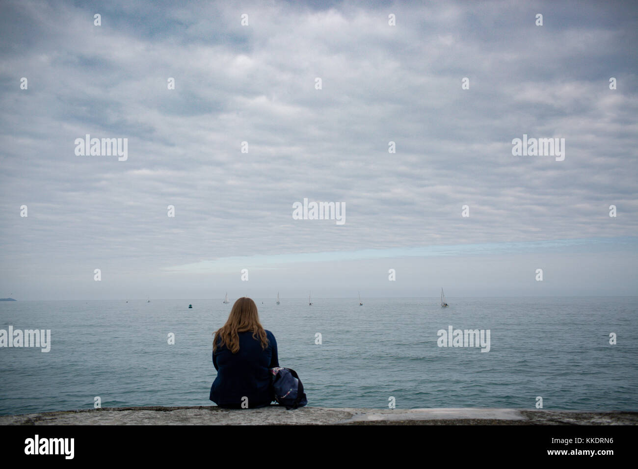 Ragazza seduta da sola su un porto di Howth è pier guardando yachts lungo il mare irlandese, la penisola di Howth, Dublino, Irlanda Foto Stock