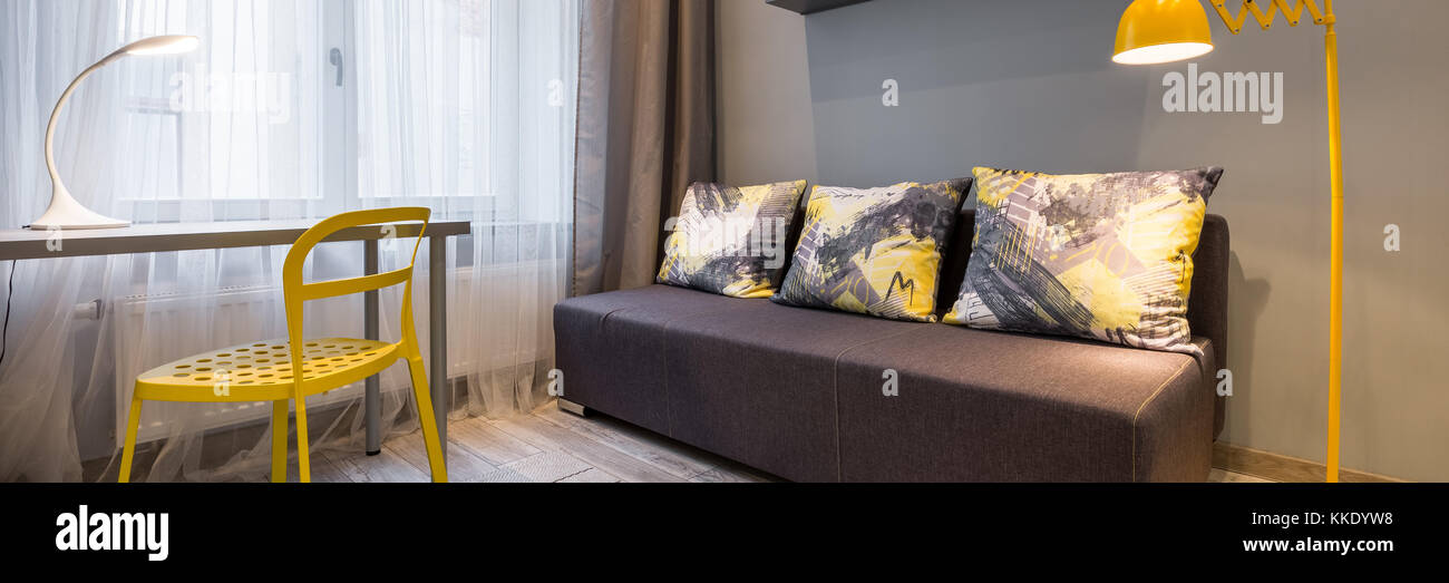 Interni semplici con divano, lampada da terra gialla, sedia e scrivania, panorama Foto Stock