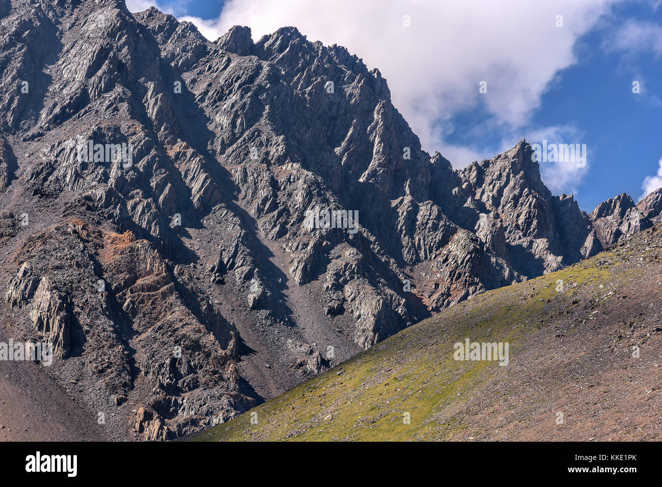 Vista panoramica sul roccioso grigio mountain top e un verde pendio di fronte ad essa sullo sfondo del cielo blu con nuvole Foto Stock