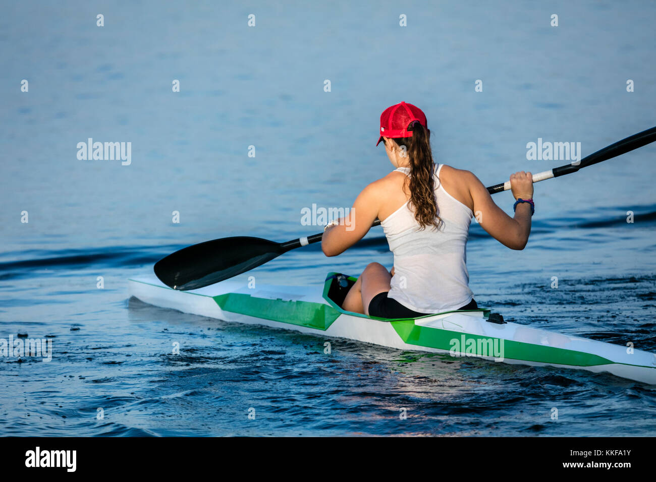 Una vista di una giovane donna sguazzare un kayak da dietro. Foto Stock