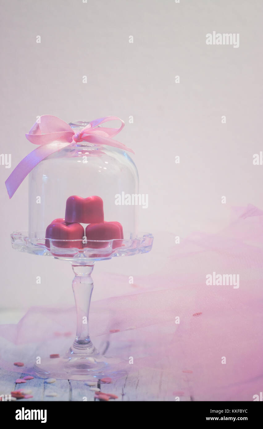 Rosa praline al cioccolato a forma di cuore, nella bella campana di vetro, bianco su sfondo di legno con spazio di copia Foto Stock