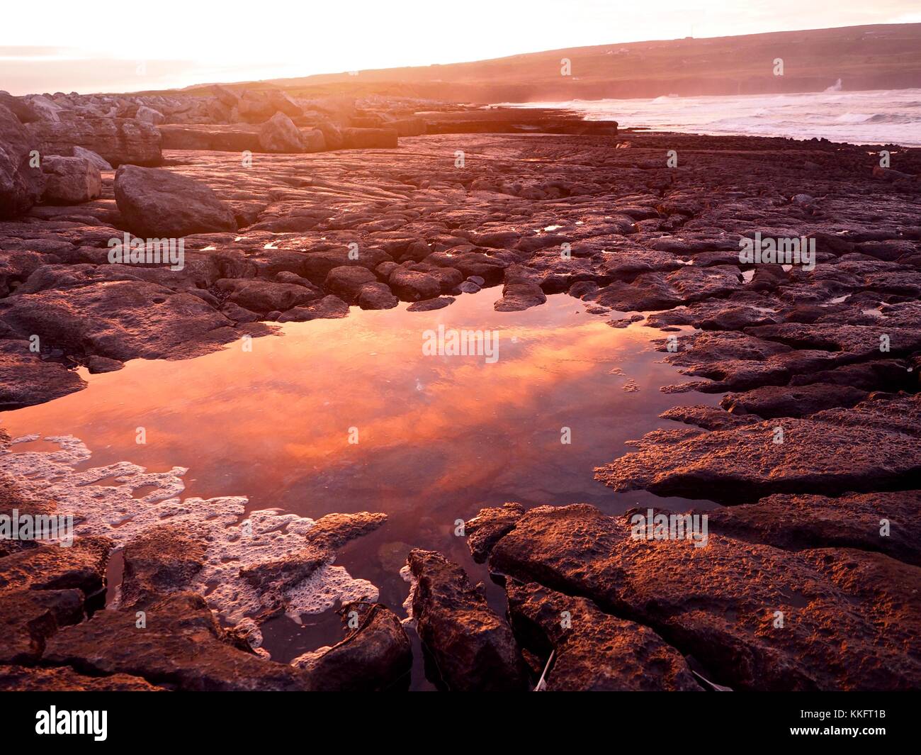 Il sole sorge su Atlantica selvaggia a modo di Doolin Pier, County Clare, Irlanda ruotando il rock pools uno squarcio di colore rosso. Foto Stock