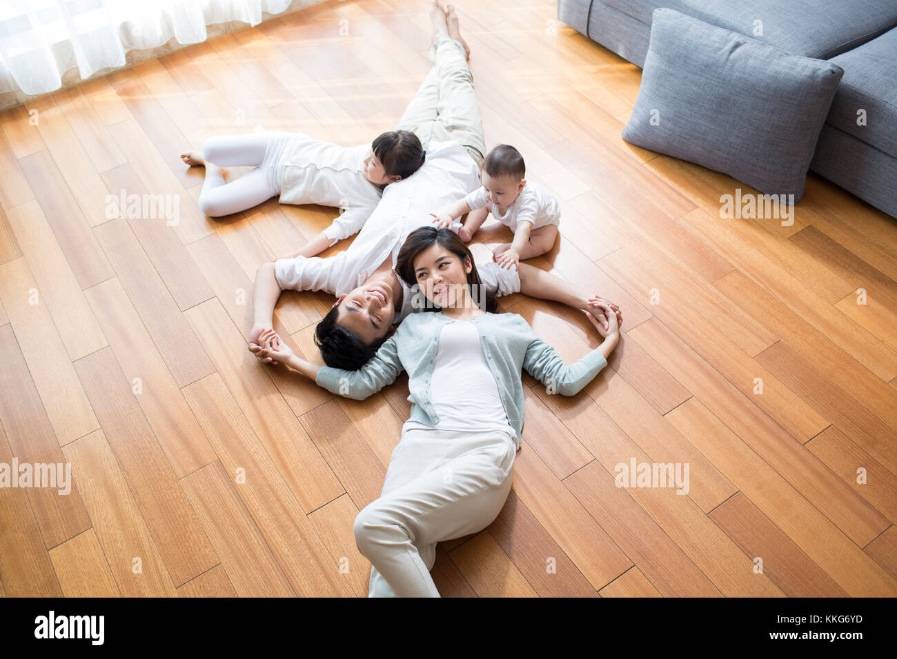 Felice giovane famiglia cinese in appoggio su pavimento in legno Foto Stock