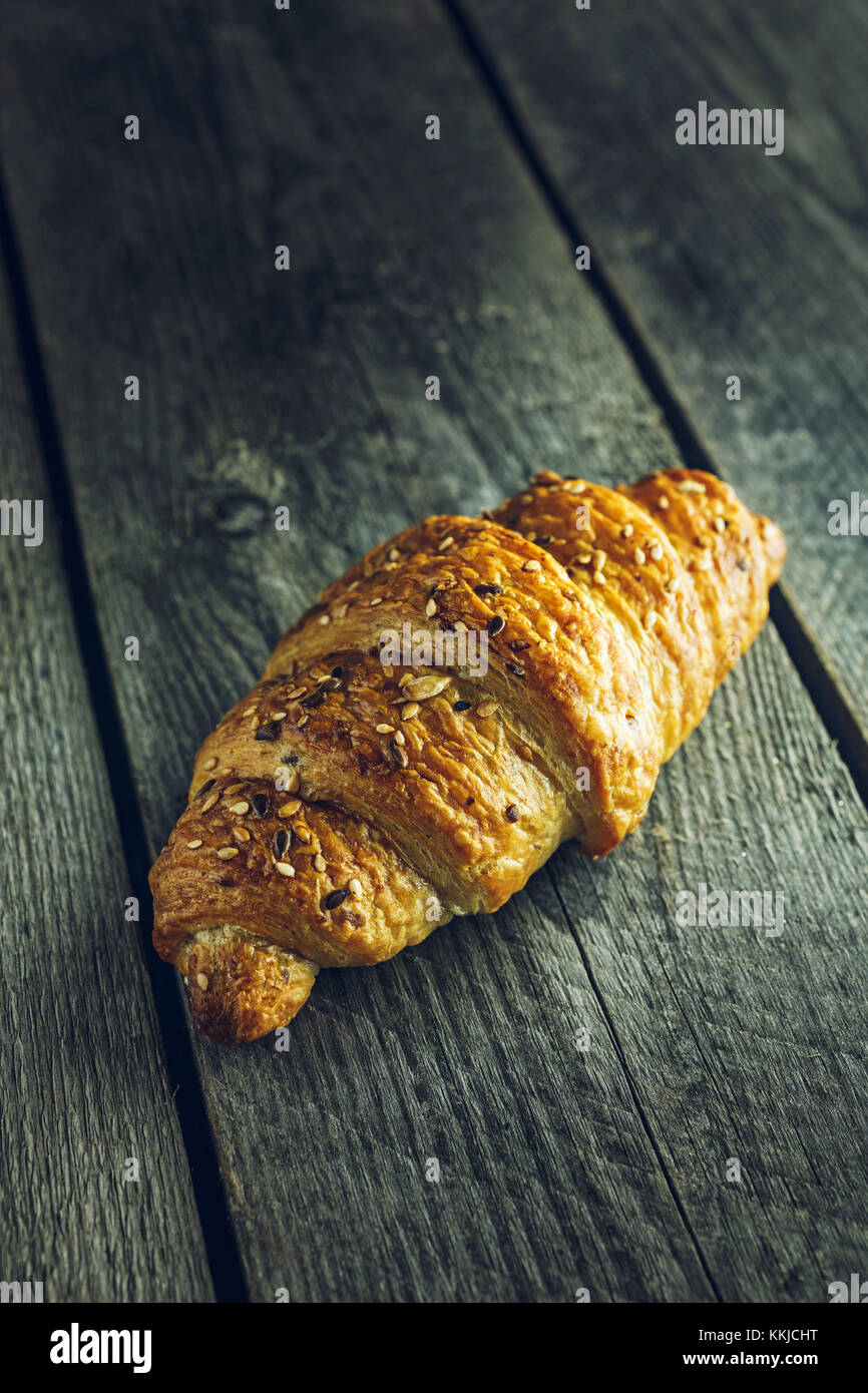 Croissant croccanti con semi su vecchio tavolo di legno Foto Stock