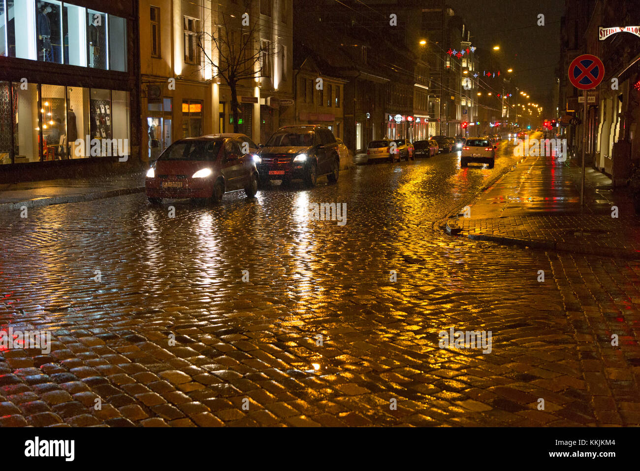 Ciottoli di notte a riga, Lettonia. Le luci si riflettono sui ciottoli bagnati dalla pioggia e dalla slitta. Foto Stock