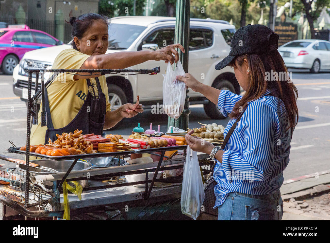 Bangkok, Tailandia. Cucina di strada fornitore che offre spiedini, Hot Dogs, arrosti di carni rosse. Foto Stock