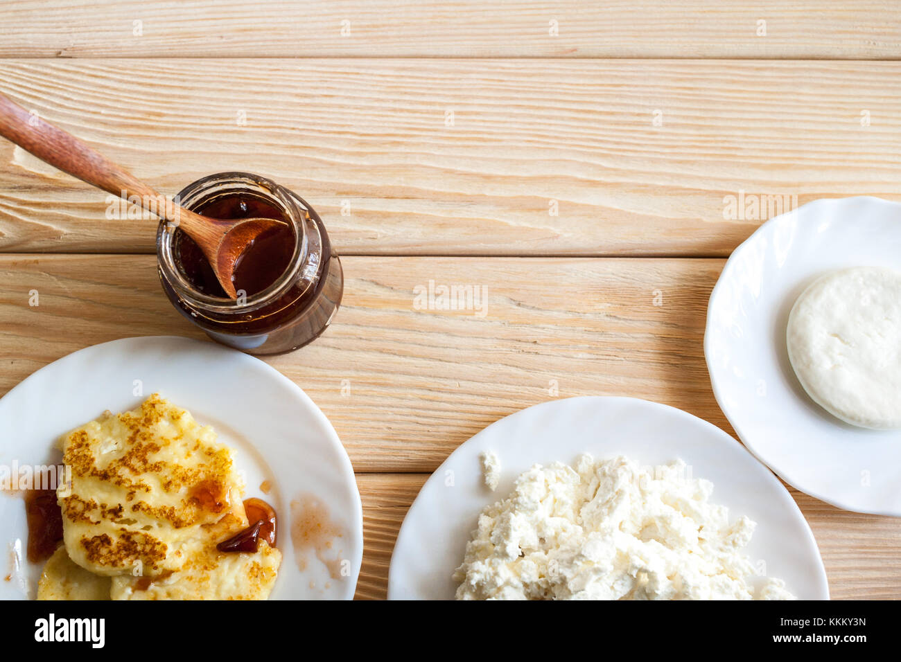 Piastre con cagliata, frittelle di formaggio a pasta morbida, cagliata fresca e confettura di prugne sono in piedi sul tavolo di legno e copia di spazio. Foto Stock