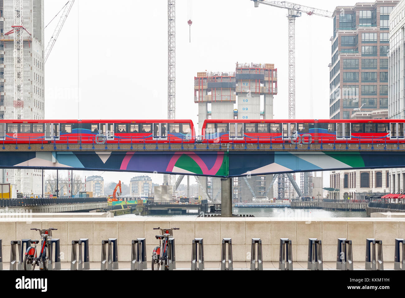 Luce treno passante per Canary Wharf a Londra con il nuovo sviluppo sito in costruzione in background Foto Stock
