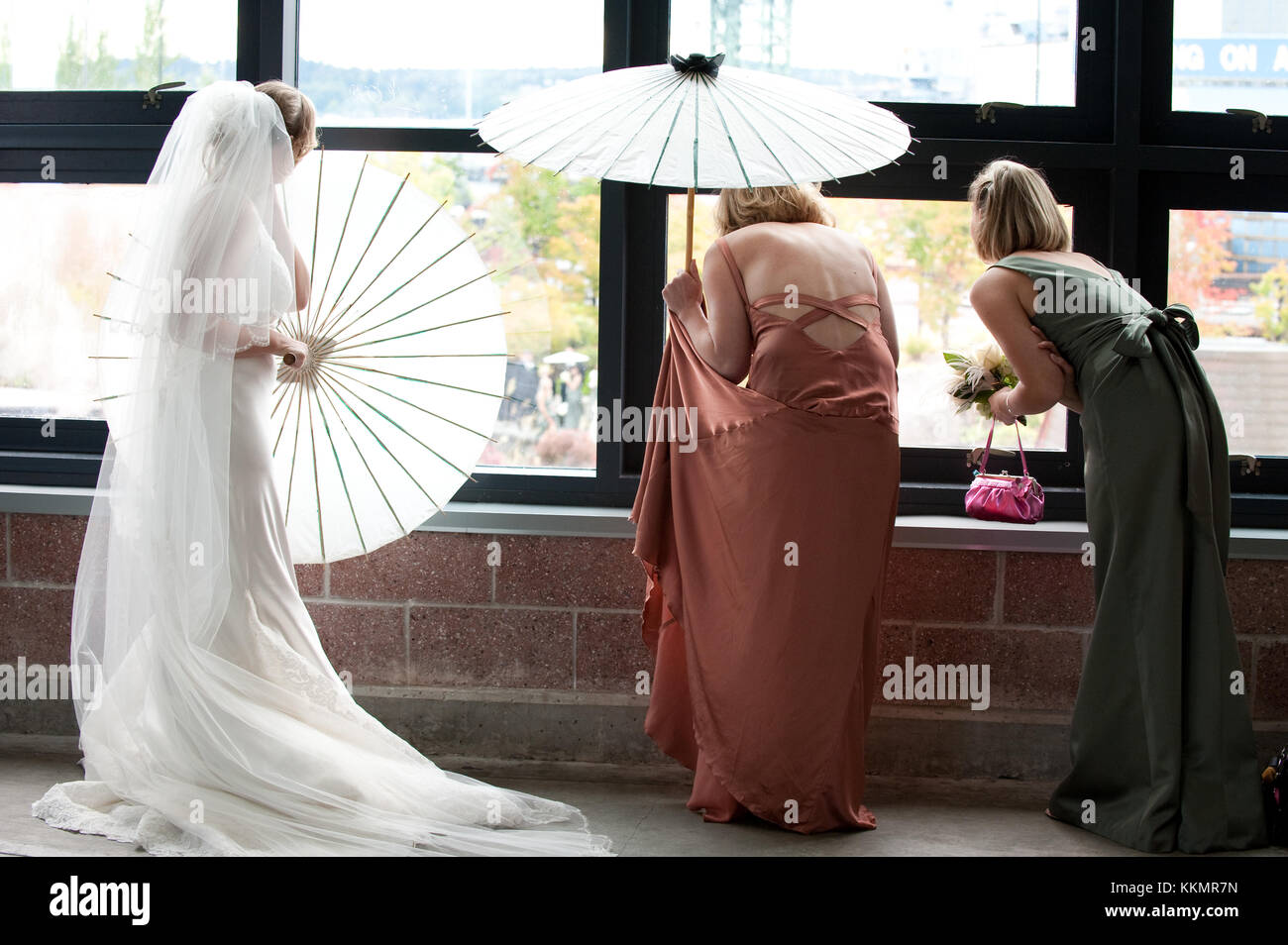 In attesa del matrimonio per iniziare, la sposa e le sue damigelle hanno due peek alla cerimonia di matrimonio all'esterno Foto Stock