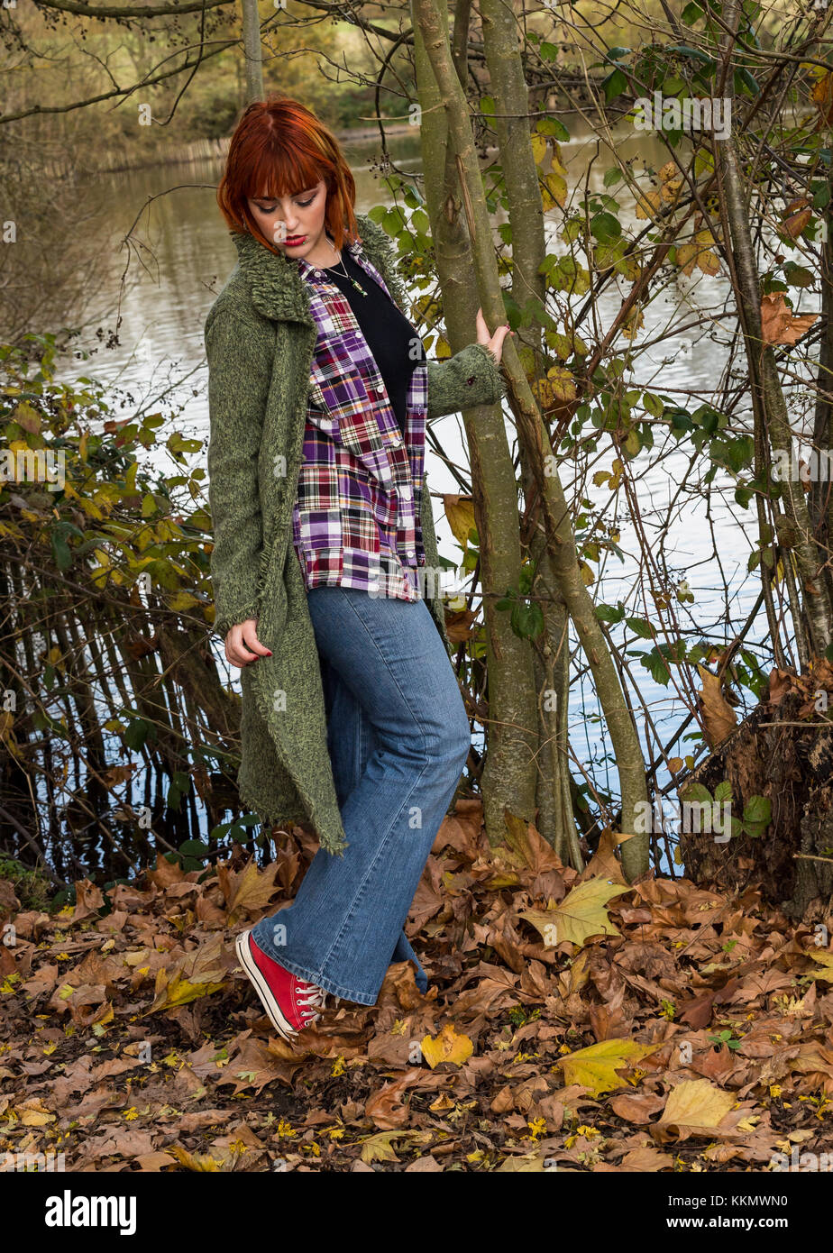 Attraente giovane donna in una impostazione paese guardando giù ai suoi piedi con alberi e lo streaming come sfondo. Foto Stock