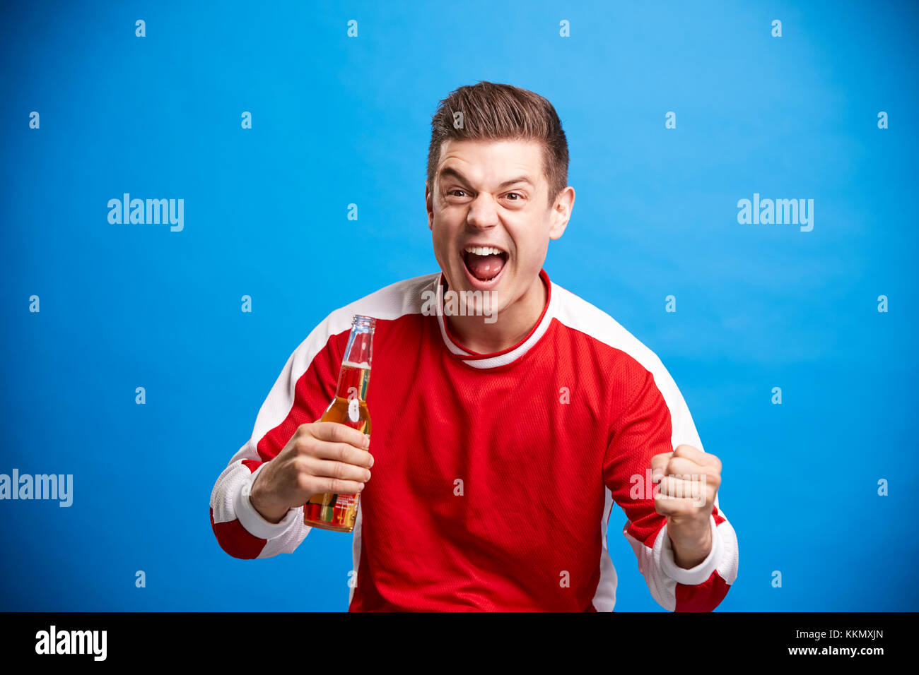 Un giovane maschio ventola sport celebrando con una bottiglia di birra Foto Stock