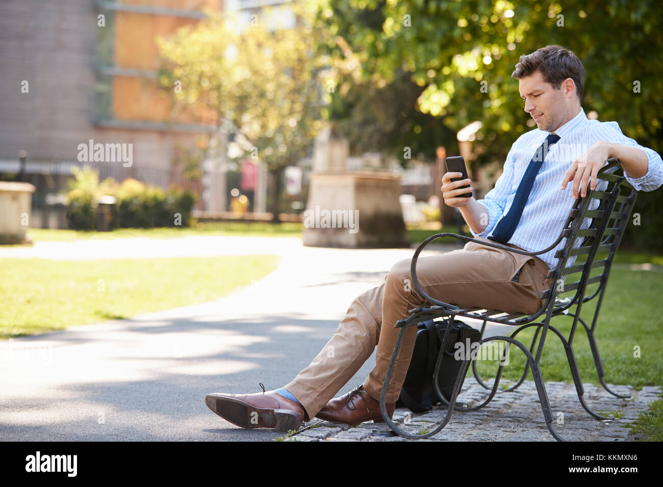 Imprenditore all'esterno utilizzando il telefono cellulare sulla pausa pranzo in posizione di parcheggio Foto Stock