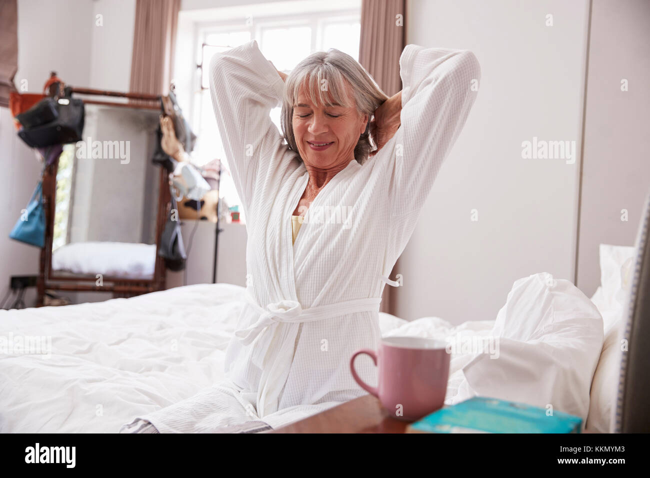 Senior donna Svegliarsi e Stretching In camera da letto Foto Stock
