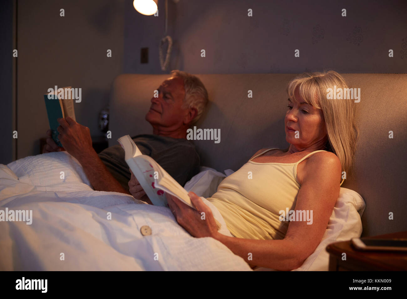 Coppia senior indossando pigiami giacente a letto la lettura Foto Stock