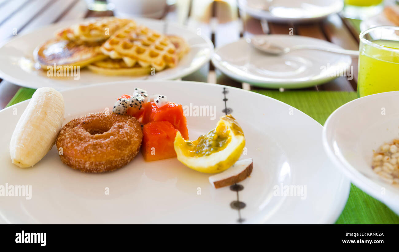 Deliziosi breaklfast sano all'aperto in un tavolo di legno. La prima colazione consiste di frutta fresca e cialde con pancake, vi è anche un succo di kiwi. Foto Stock