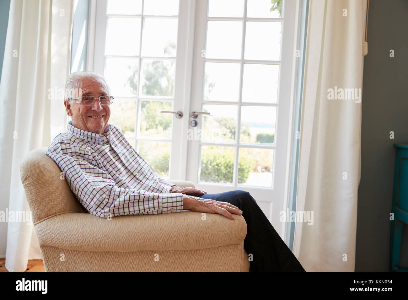 Senior uomo seduto in poltrona diventa sorridente alla fotocamera Foto Stock
