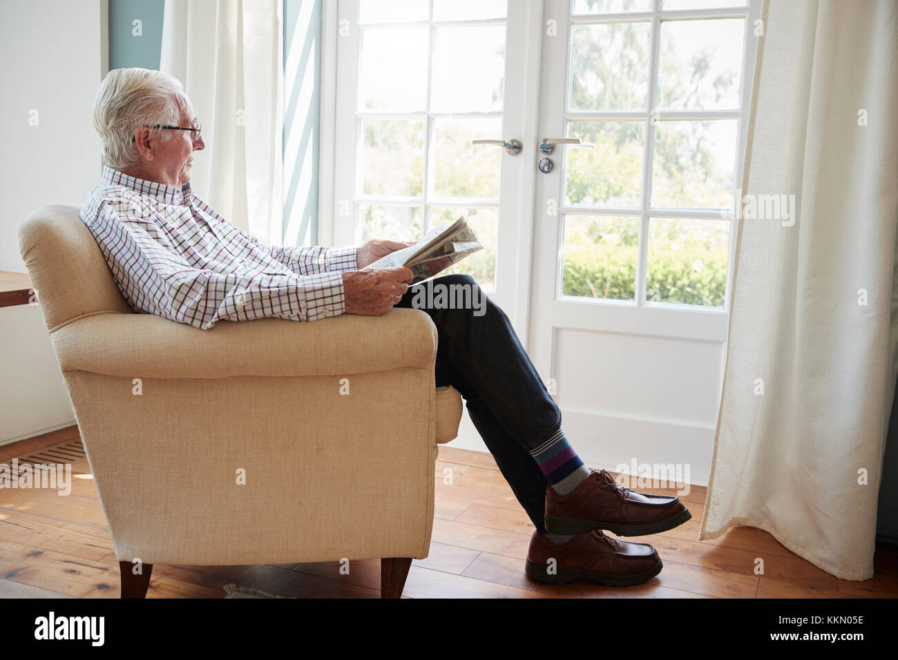 Senior uomo seduto in poltrona leggendo il giornale a casa Foto Stock