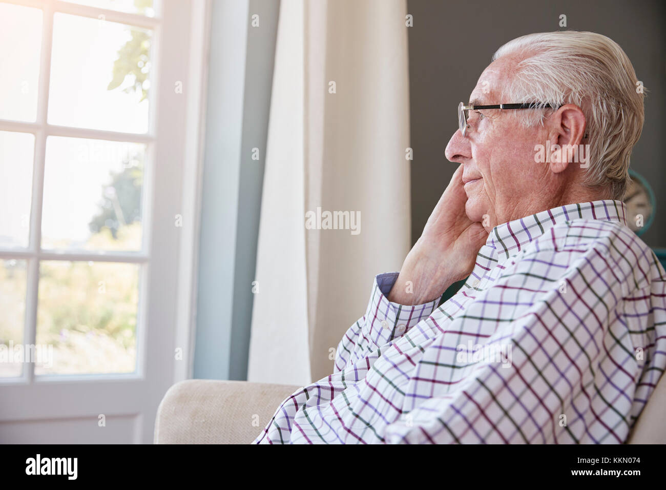 Senior uomo si siede guardando fuori della finestra a casa Foto Stock
