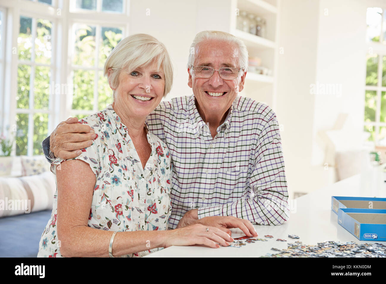 Coppia senior facendo un puzzle a casa, sorridente alla fotocamera Foto Stock