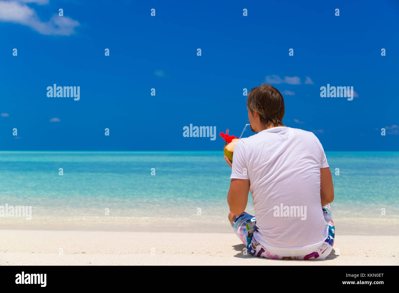 Uomo seduto in spiaggia mentre si beve acqua di cocco e rilassarsi. Foto Stock
