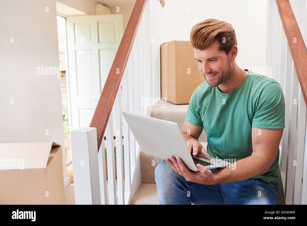 Uomo che si muove nella nuova casa guardando le finanze personali sul computer portatile Foto Stock