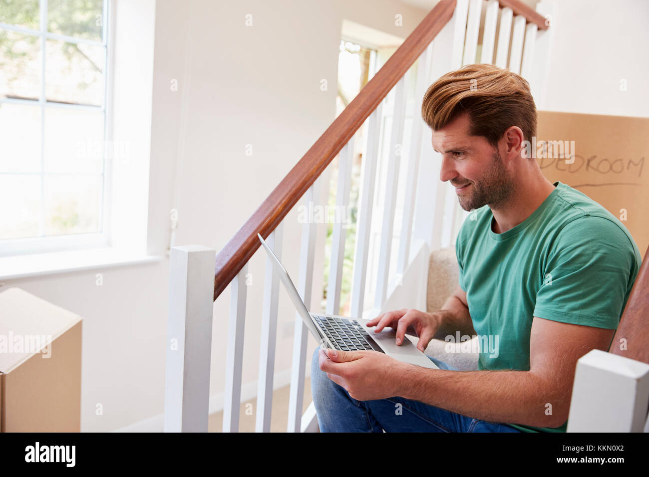 Uomo che si muove nella nuova casa guardando le finanze personali sul computer portatile Foto Stock