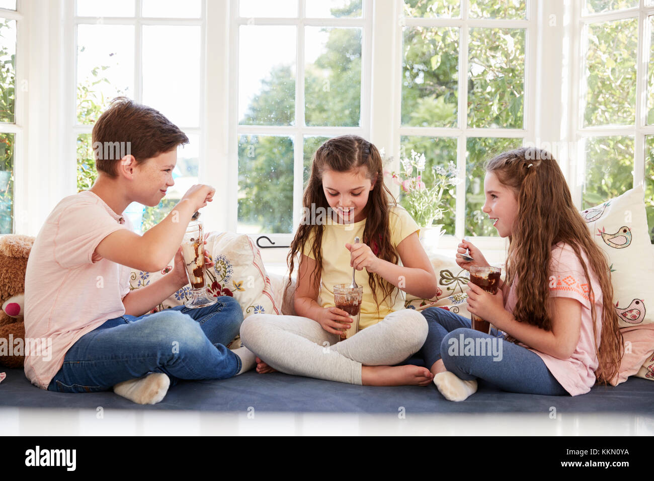 I bambini seduti sul sedile della finestra a mangiare il gelato Sundaes Foto Stock