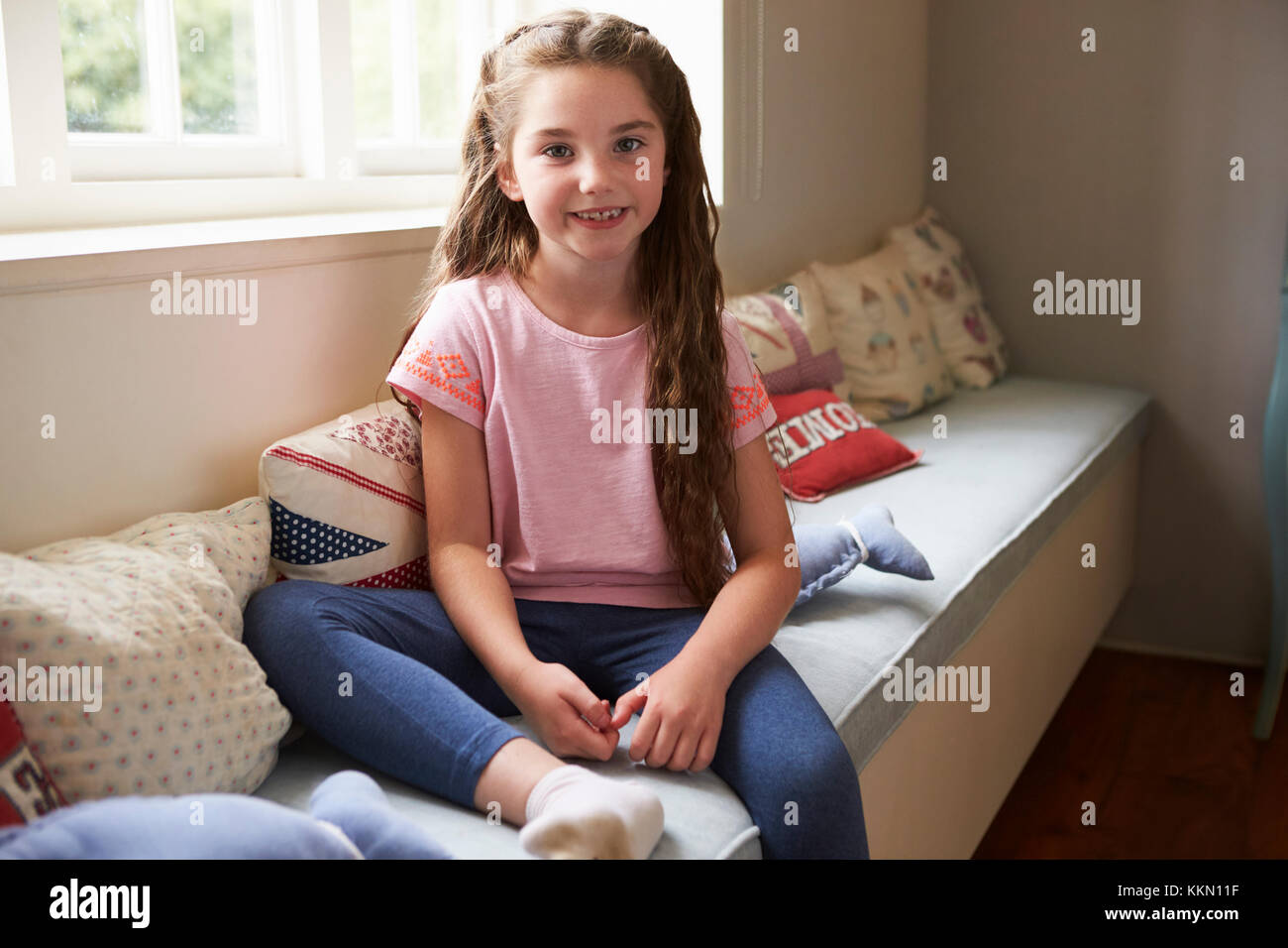 Ritratto di giovane sorridente ragazza seduta sul sedile della finestra a casa Foto Stock