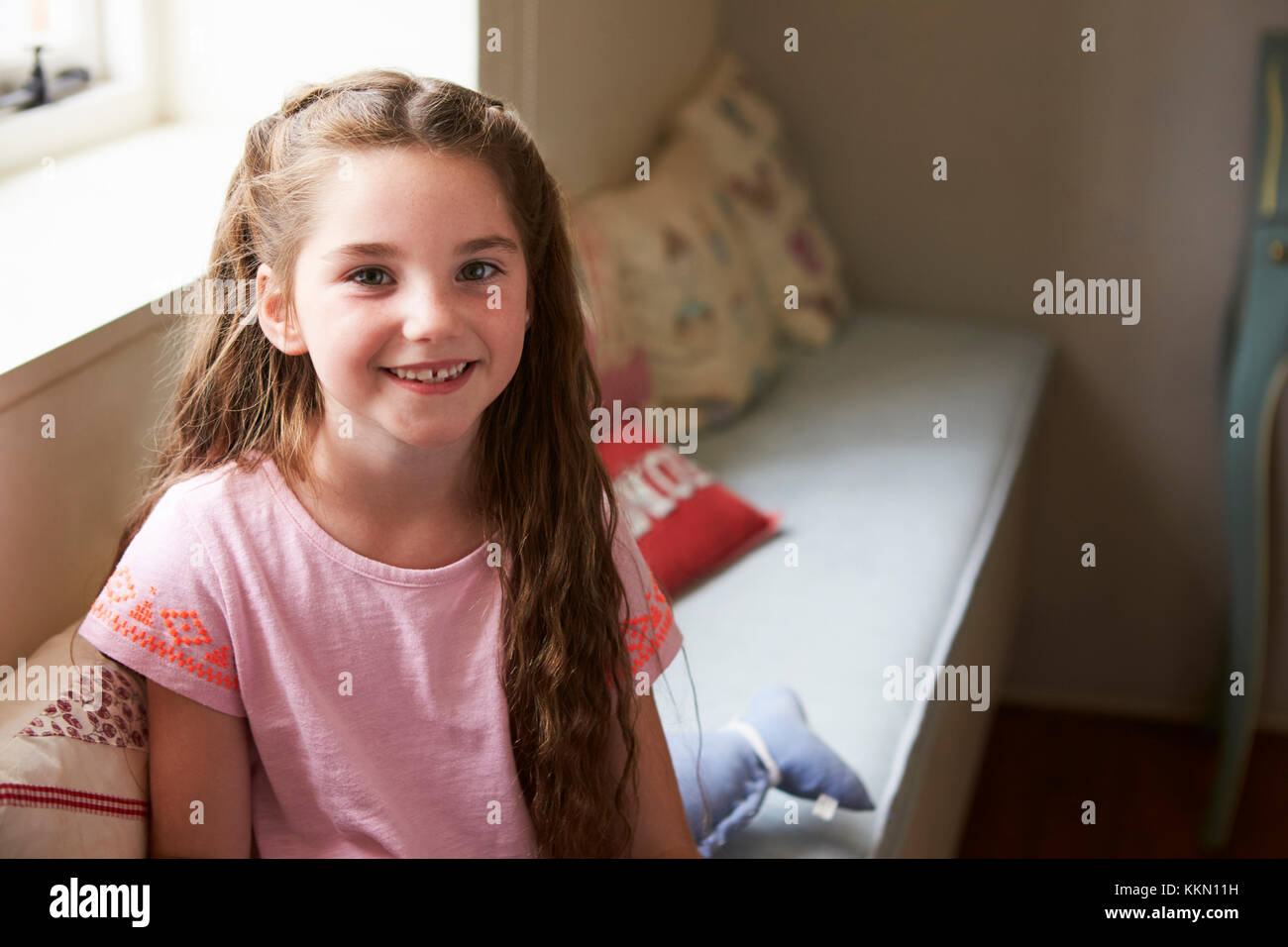 Ritratto di giovane sorridente ragazza seduta sul sedile della finestra a casa Foto Stock