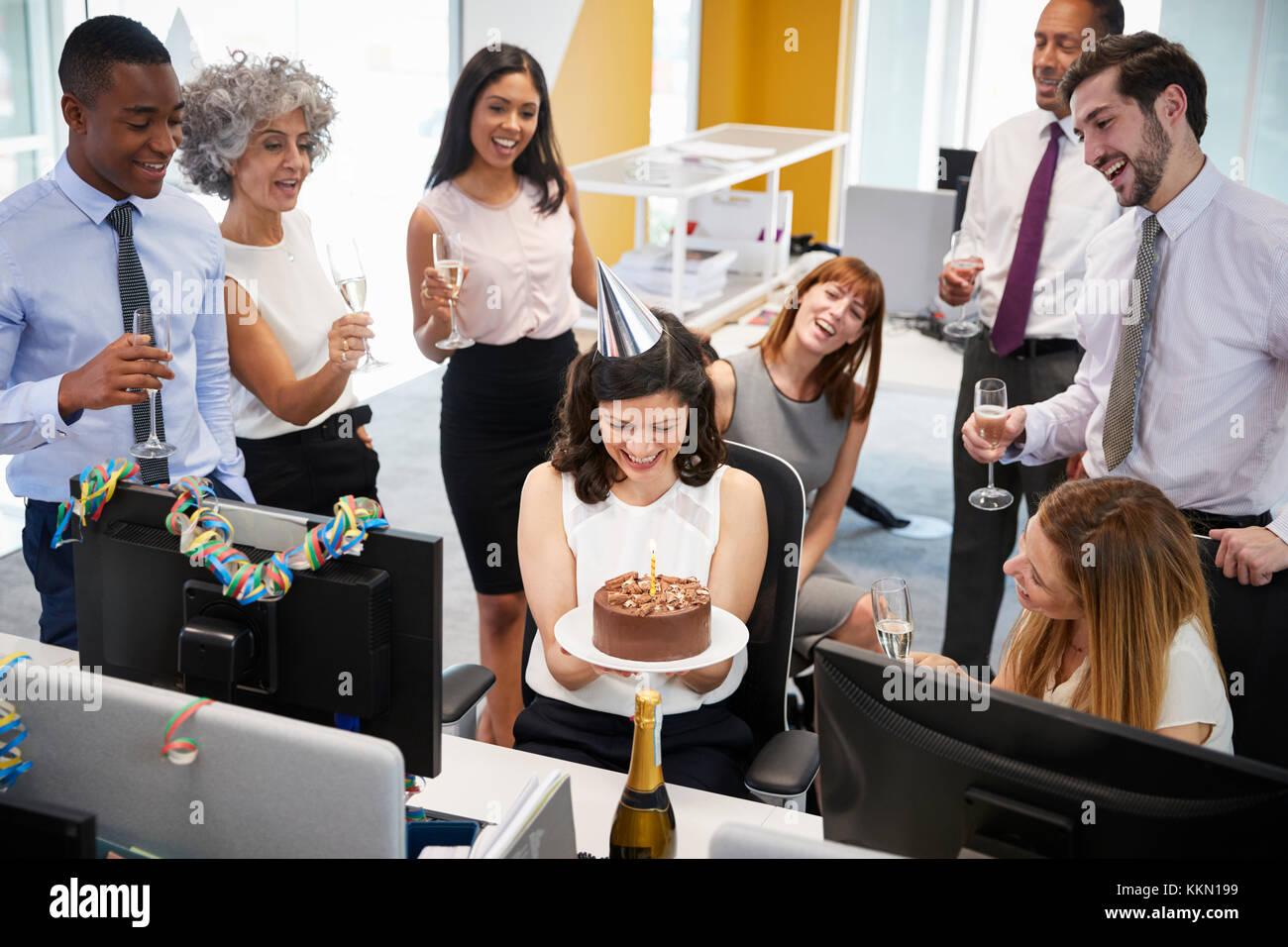 I colleghi si sono riuniti presso la donna alla scrivania per festeggiare un compleanno Foto Stock