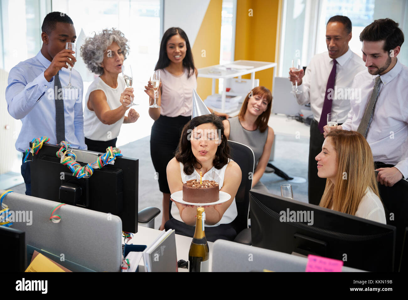 I colleghi si sono riuniti presso la donna alla scrivania per festeggiare un compleanno Foto Stock
