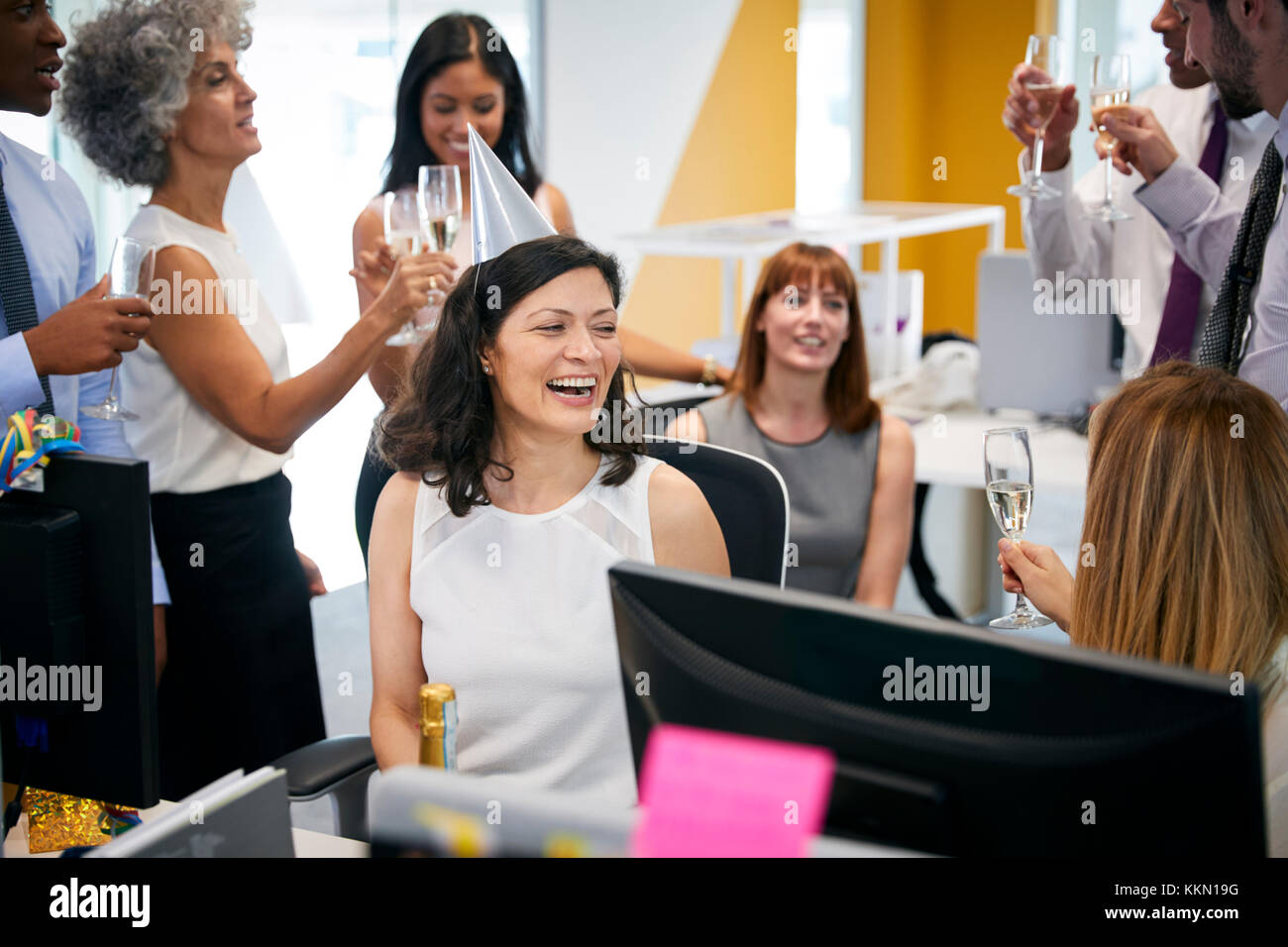 I colleghi si sono riuniti presso la donna alla scrivania per festeggiare un compleanno Foto Stock