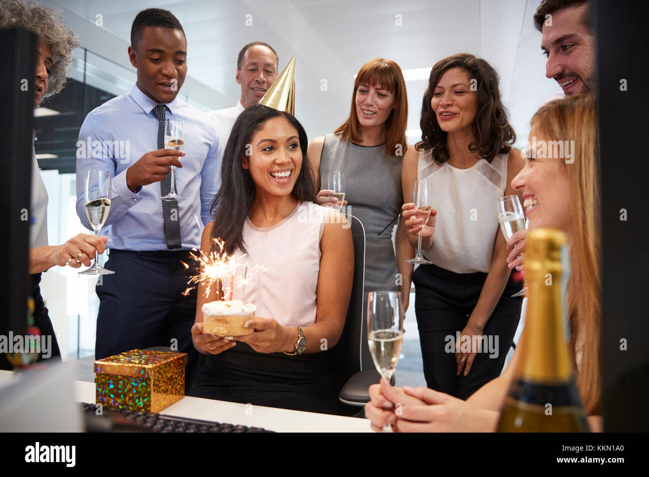 I colleghi si sono riuniti presso la donna alla scrivania per festeggiare un compleanno Foto Stock