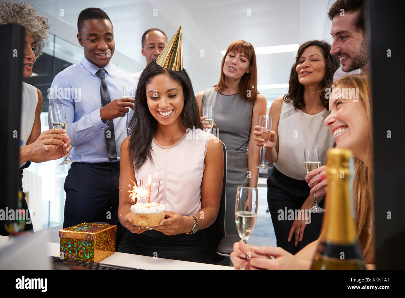 I colleghi si sono riuniti presso la donna alla scrivania per festeggiare un compleanno Foto Stock