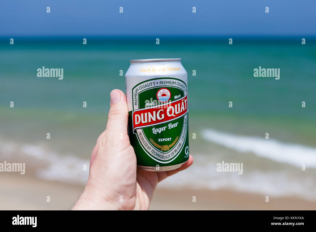 Hoi An, vietnam - marzo 15 2017: mano azienda può di sterco di freddo quat birra contro Smeraldo oceano e cielo blu Foto Stock