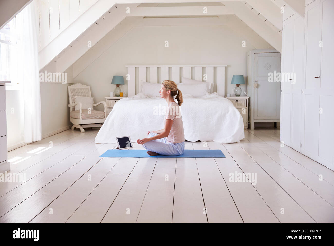 Donna con tavoletta digitale utilizzando la meditazione di app in camera da letto Foto Stock