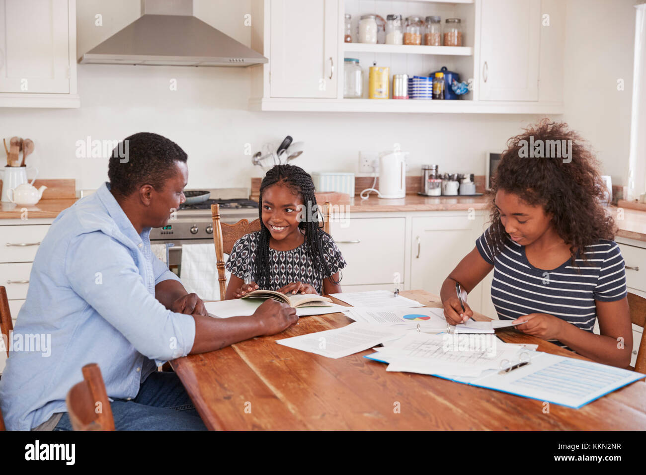 Aiutando il padre di due figlie seduta a tavola facendo i compiti di scuola Foto Stock