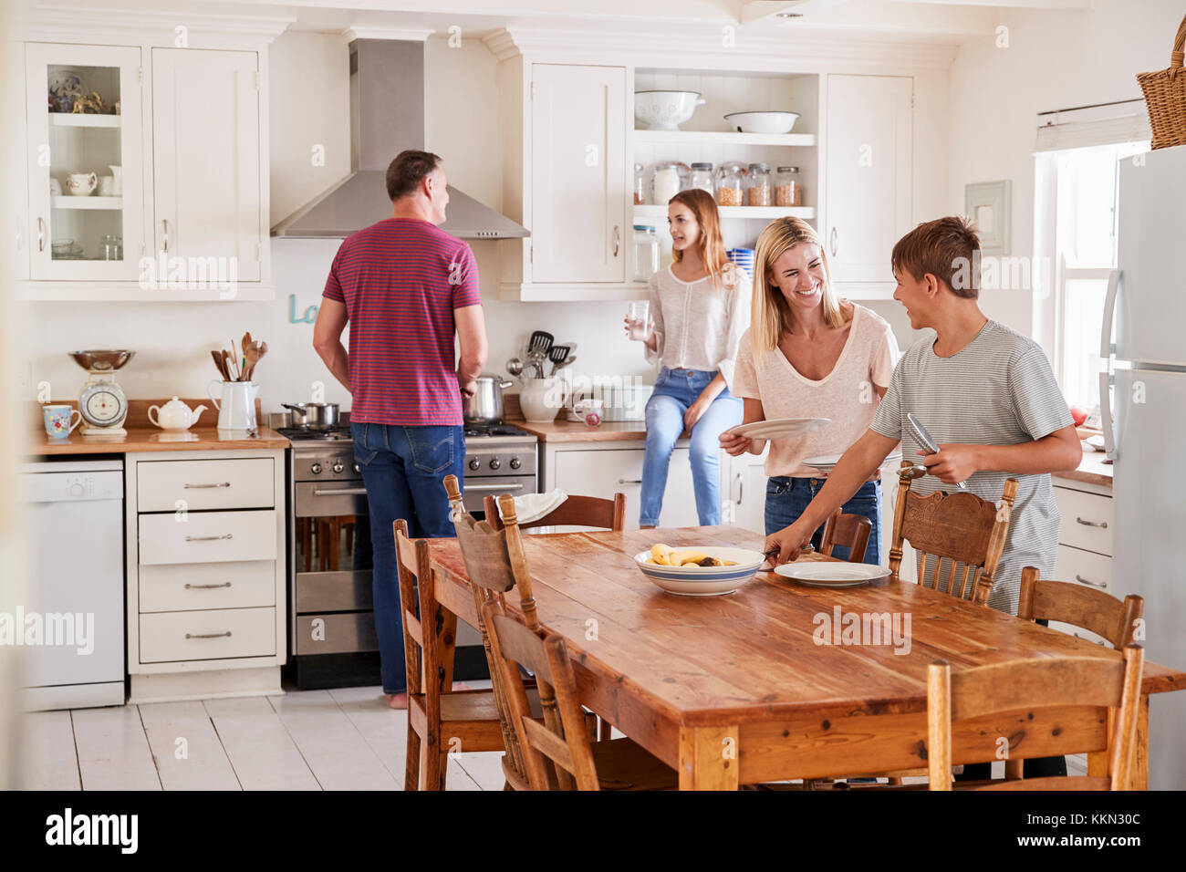 Famiglia con figli adolescenti che stabilisce la tabella per il pasto in cucina Foto Stock