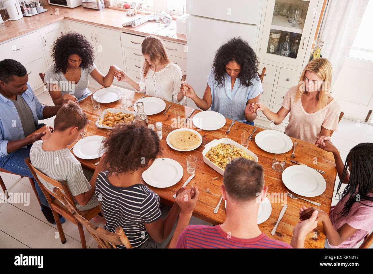 Due famiglie dicendo grazia prima di mangiare mangiare insieme Foto Stock