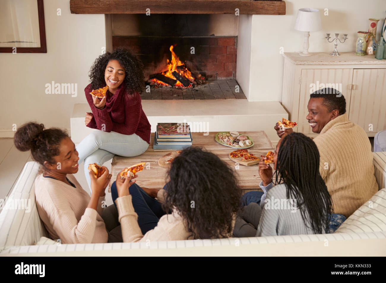 Famiglia seduto sul divano nel salone accanto al caminetto di mangiare la pizza Foto Stock