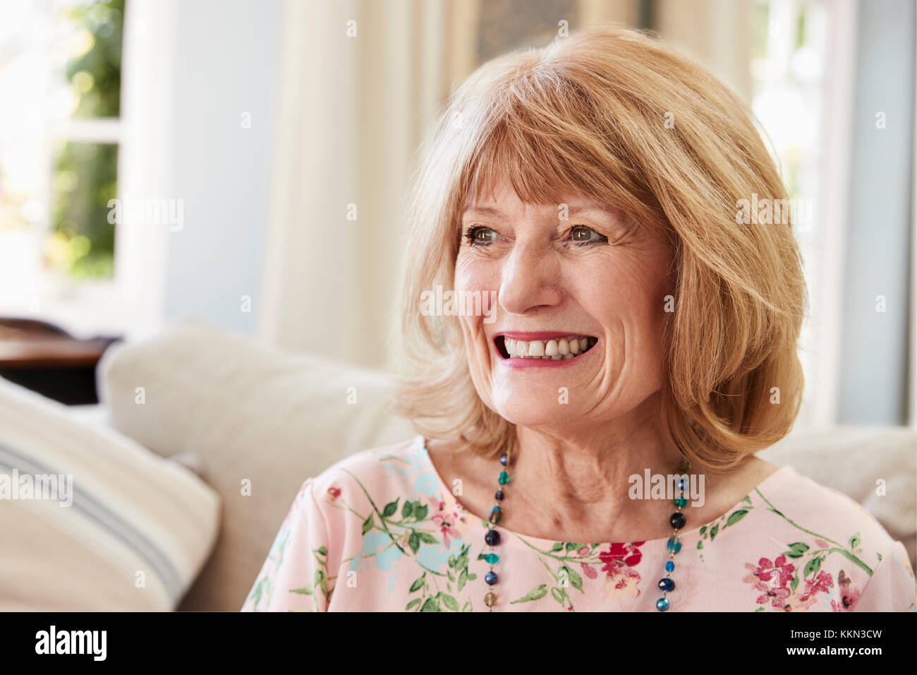 Senior sorridente donna seduta sul divano di casa Foto Stock