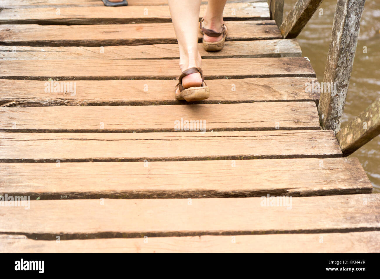 Piedi femminili in sandali che calpestano una barriera di legno (un ponte pedonale) che attraversa l'acqua a Ssezibwa Falls Uganda. Foto scattata il 23 2017 aprile. Foto Stock