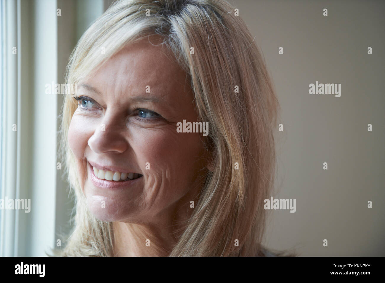 Sorridente donna matura in piedi accanto alla finestra Foto Stock