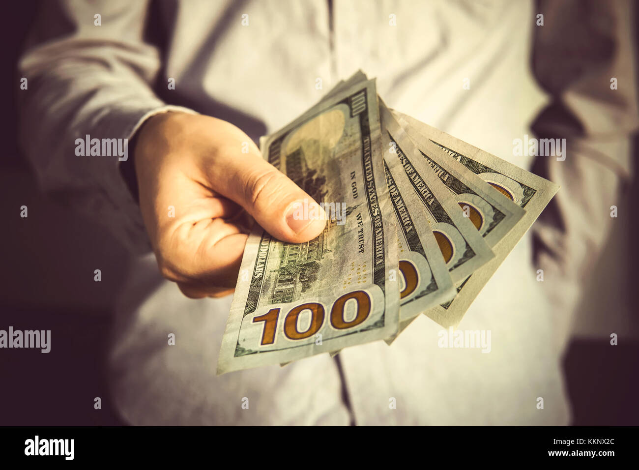 Uomo in una tuta mantenendo la ventola del dollaro banconote. un commerciante tiene fuori una tangente di 500 dollari Foto Stock