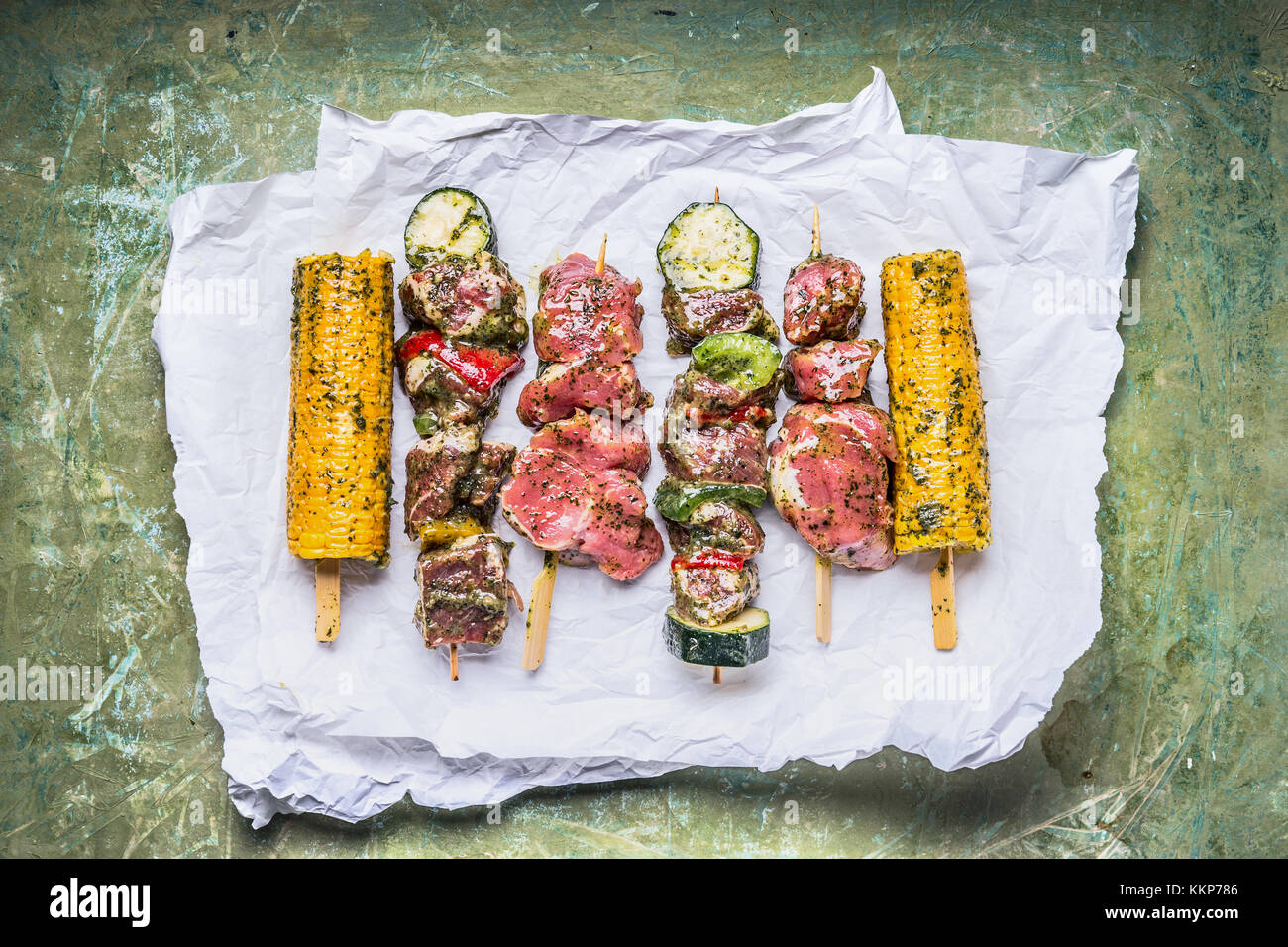 Varie gli spiedini di carne per grill con verdure , le pannocchie e condimento su verde sfondo rustico , vista superiore Foto Stock