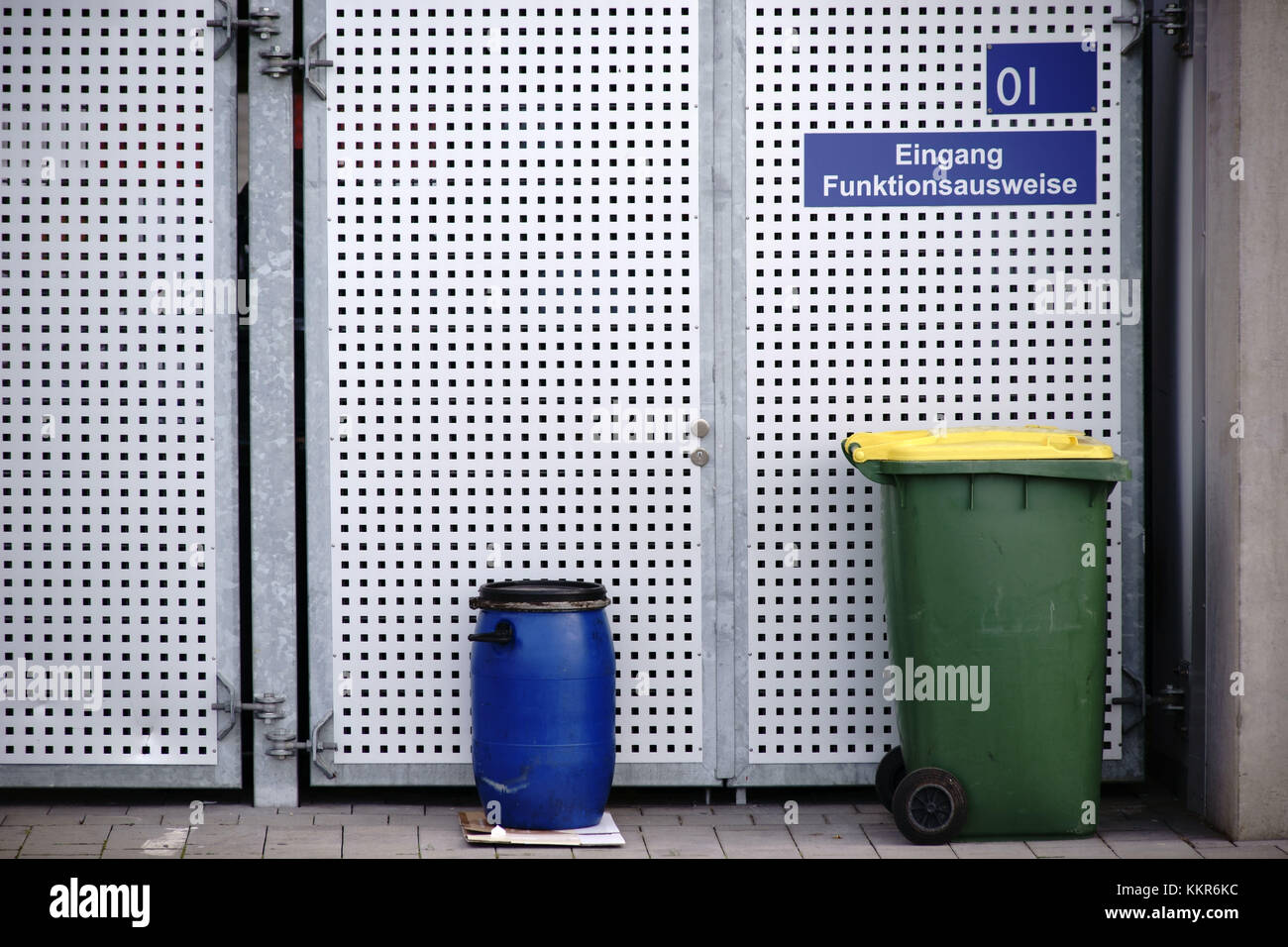 Contenitori per i rifiuti in piedi di fronte a un (paled) cancello realizzato in lamiera forata. Foto Stock